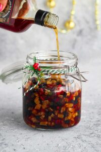 Pouring rum over the dry fruits placed in a glass jar