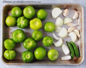 Tomatillos, garlic, serrano peppers and onion on a baking sheet.