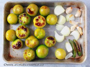 Broiled tomatillos, garlic, serrano peppers and onion on a baking sheet.