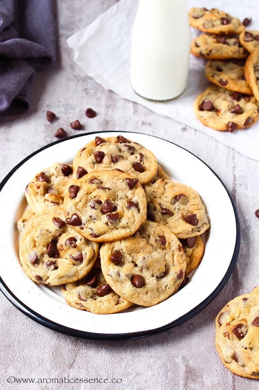 Egg-free chocolate chip cookies in a white rimmed plate with some cookies in the background along with a bottle of milk.