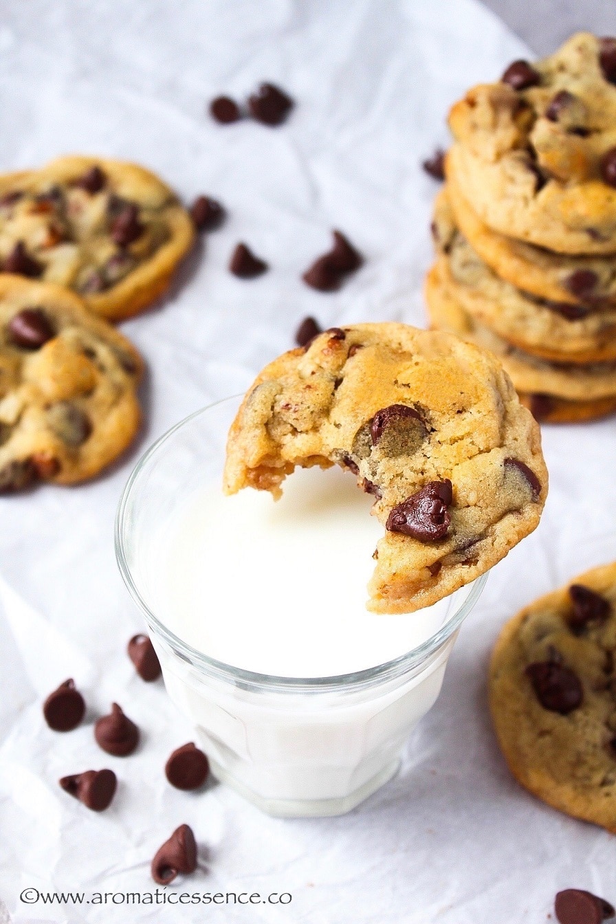 Chocolate chip cookie resting on the edge of a glass of milk.