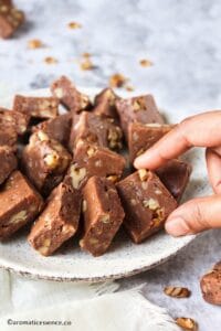 Picking up a pice of walnut toffee/fudge from a plate.