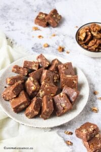 Walnut fudge arranged in a white speckled plate with a bowl of walnuts in the background.