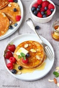 Three pancakes stacked in a white rimmed plate topped with butter, syrups, and berries