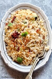Bagara annam served in an oval pewter tray garnished with brown onions and mint leaves