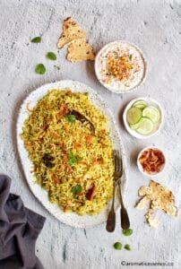 Mint rice served in a deshaped oval platter served along with sliced English cucumber, boondi raita, and papad