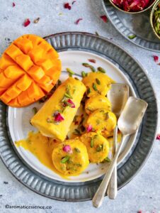 Two aam kulfi's on a marble plate, one whole and one sliced into discs