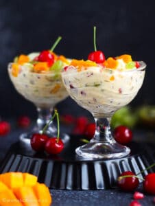 Two dessert bowls filled with creamy fruit salad, topped with assorted fruits