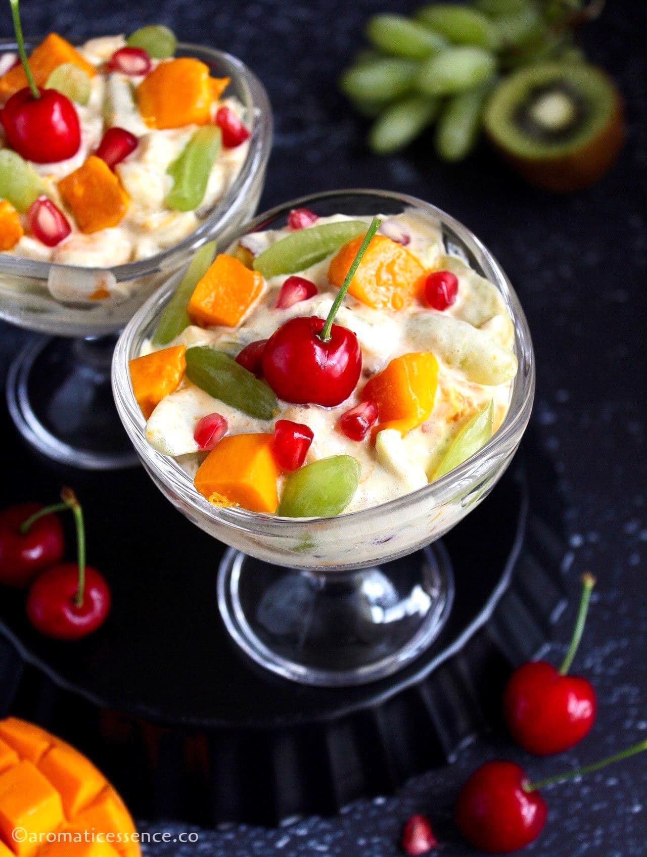 45 degree angle shot of creamy fruit salad in two dessert bowls placed on an inverted black fluted pan