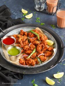 Chicken pakodi garnished with fried green chilies and curry leaves, served in a galvanized rimmed plate