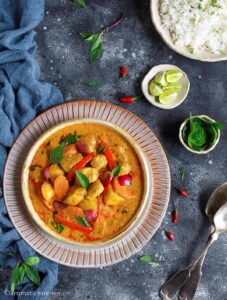 Yellow Thai chicken curry garnished with fresh Thai basil leaves, served in a white shallow bowl