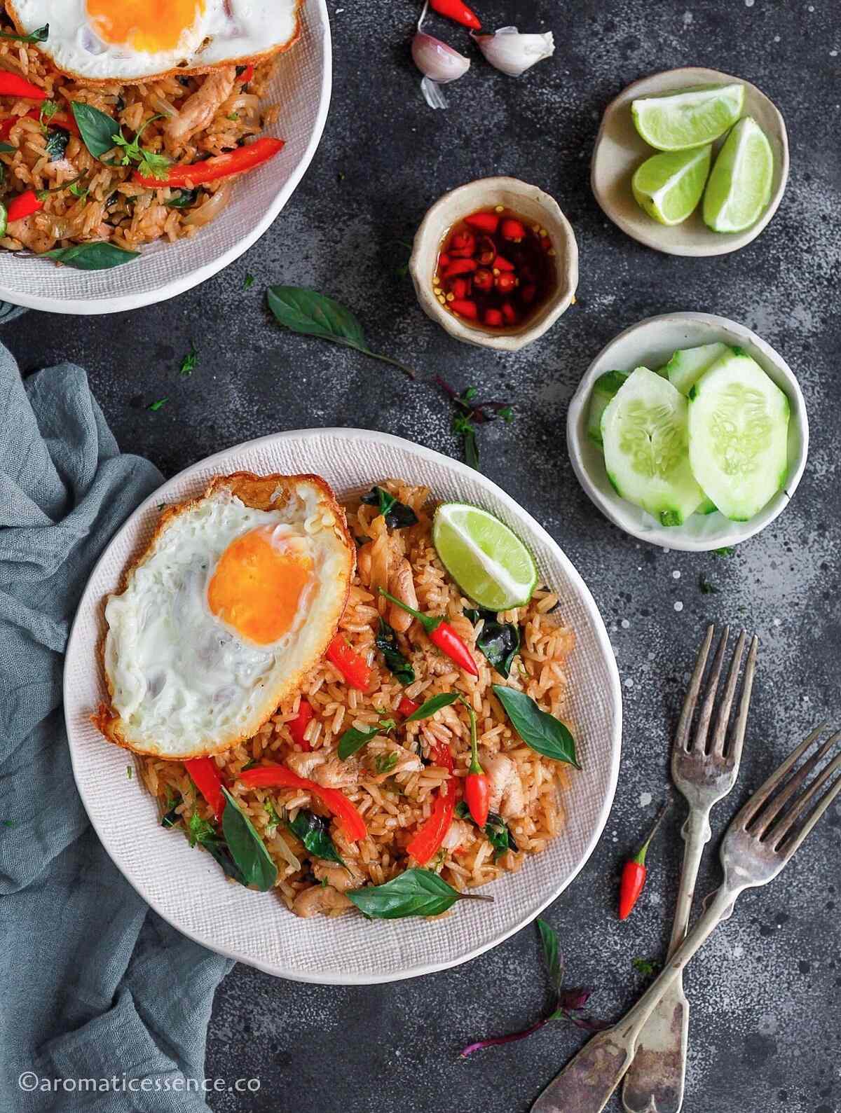 Thai basil fried rice with chicken served in two shallow ceramic white bowls against a dark background
