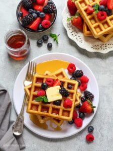 Eggless waffles topped with butter and berries, drizzled with maple syrup