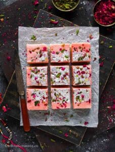 9 pieces of coconut burfi squares placed on a parchment paper over a wooden serving board