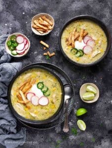 Overhead shot of green chicken enchilada soup served in 2 black bowls