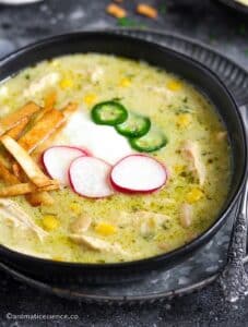 Close-up shot of Instant Pot green enchilada chicken soup topped with baked tortilla strips, jalapenos, sliced radishes, and sour cream