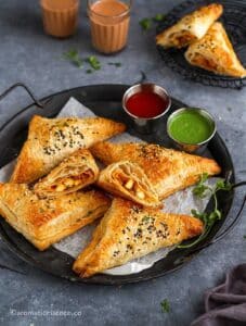 Paneer puff served in a black galvanized tray along with ketchup and green chutney