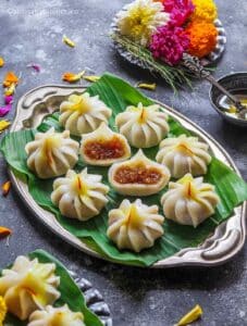 A modak cut in half placed on a silver platter along with more steamed modak's