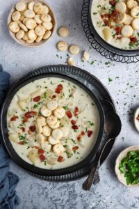 Overhead shot of Instant Pot clam chowder served in a black bowl topped with oyster cracker, crispy bacon bits, and chopped parsley
