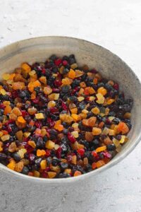 45 degree angle shot of mixed dry fruits, candied fruits, candied orange peel and candied ginger in a round grey ceramic bowl