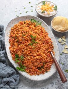 45 degree angle shot of South Indian tomato rice served with boondi raita and papadum