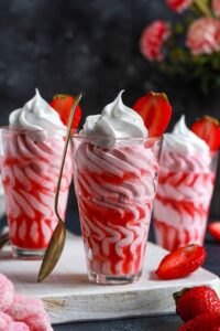 Strawberry mousse served in 3 glasses topped with whipped cream and fresh strawberry halves